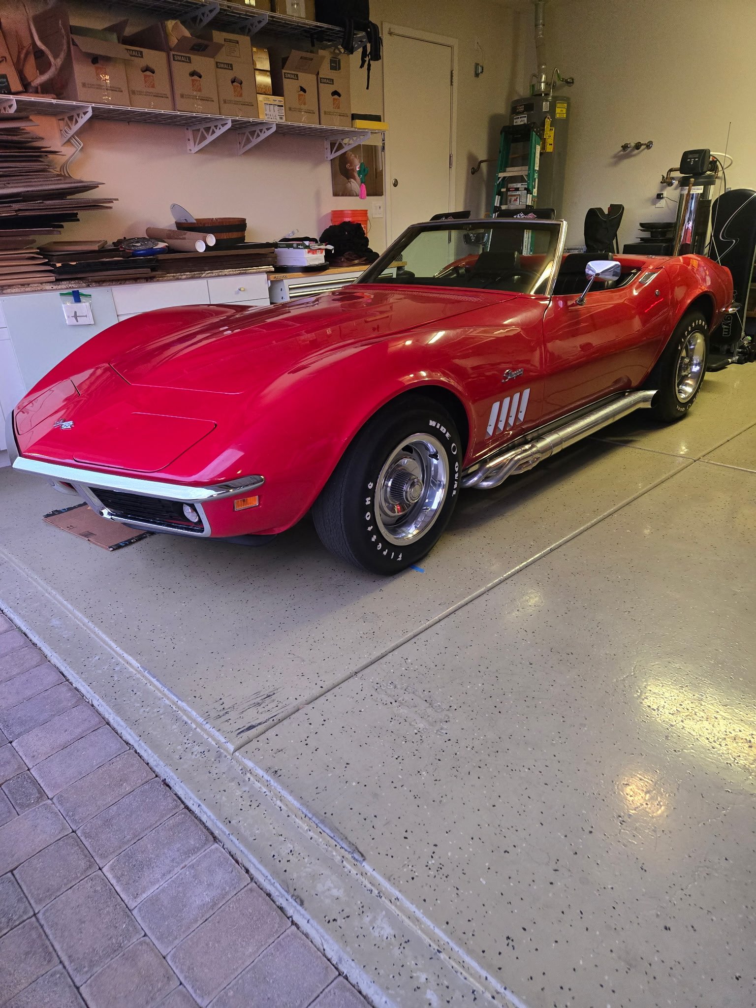 Restored red Corvette convertible parked in ShuBrews Garage Bar workshop with tools and equipment visible in background.