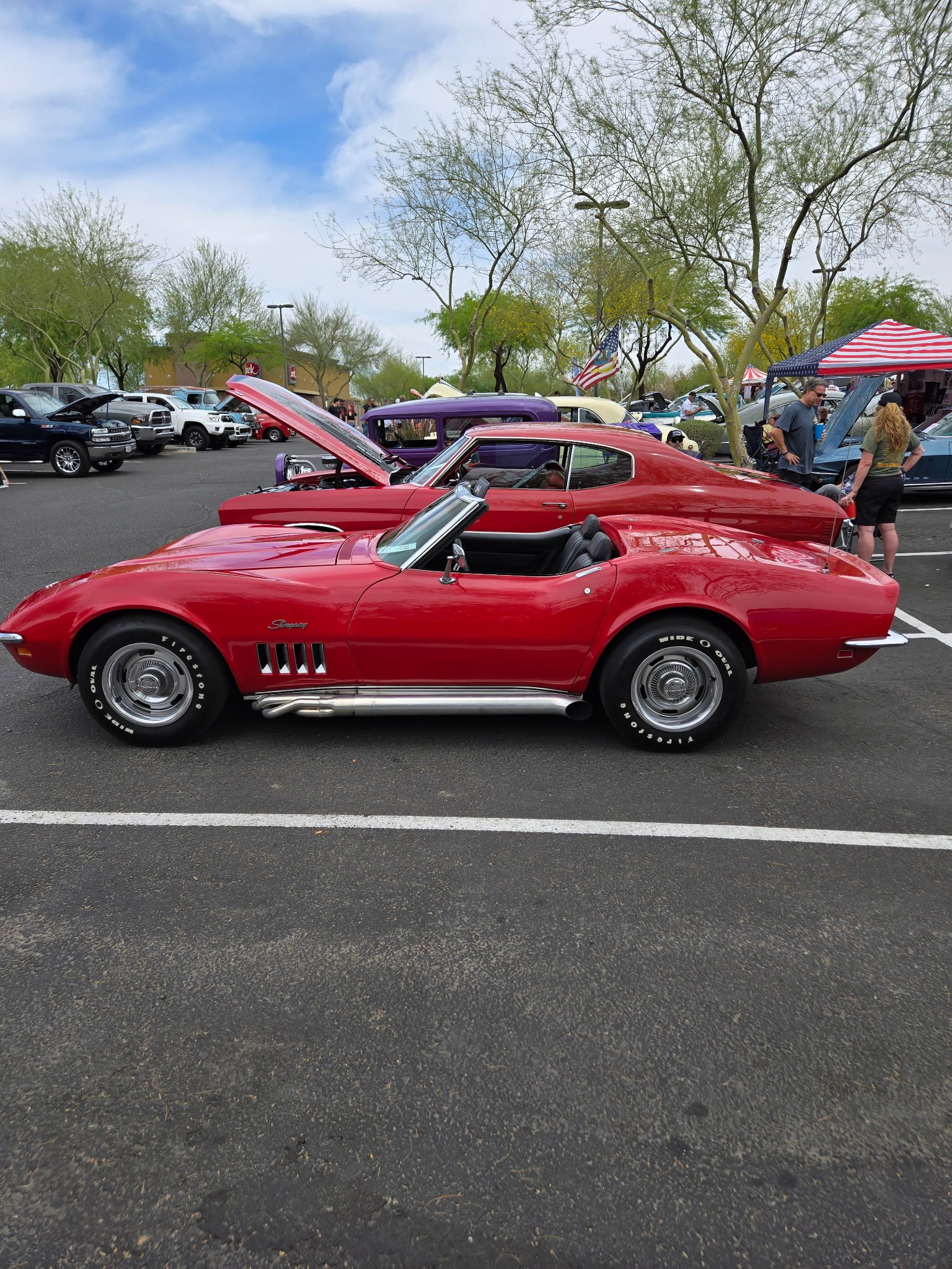 Classic red Corvette convertible with hood open displayed at outdoor car show in Phoenix.