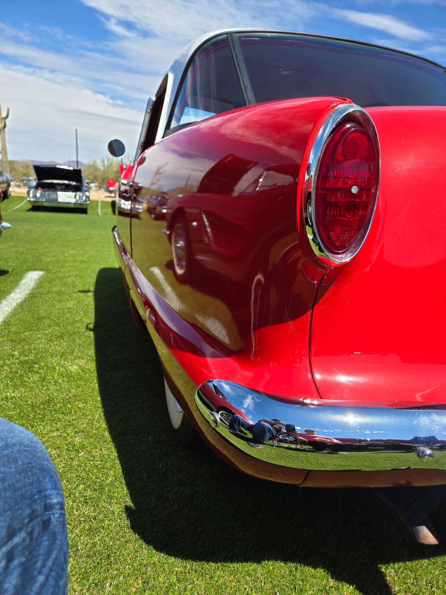 Classic red and blue vintage car displayed at outdoor car show on grass field.