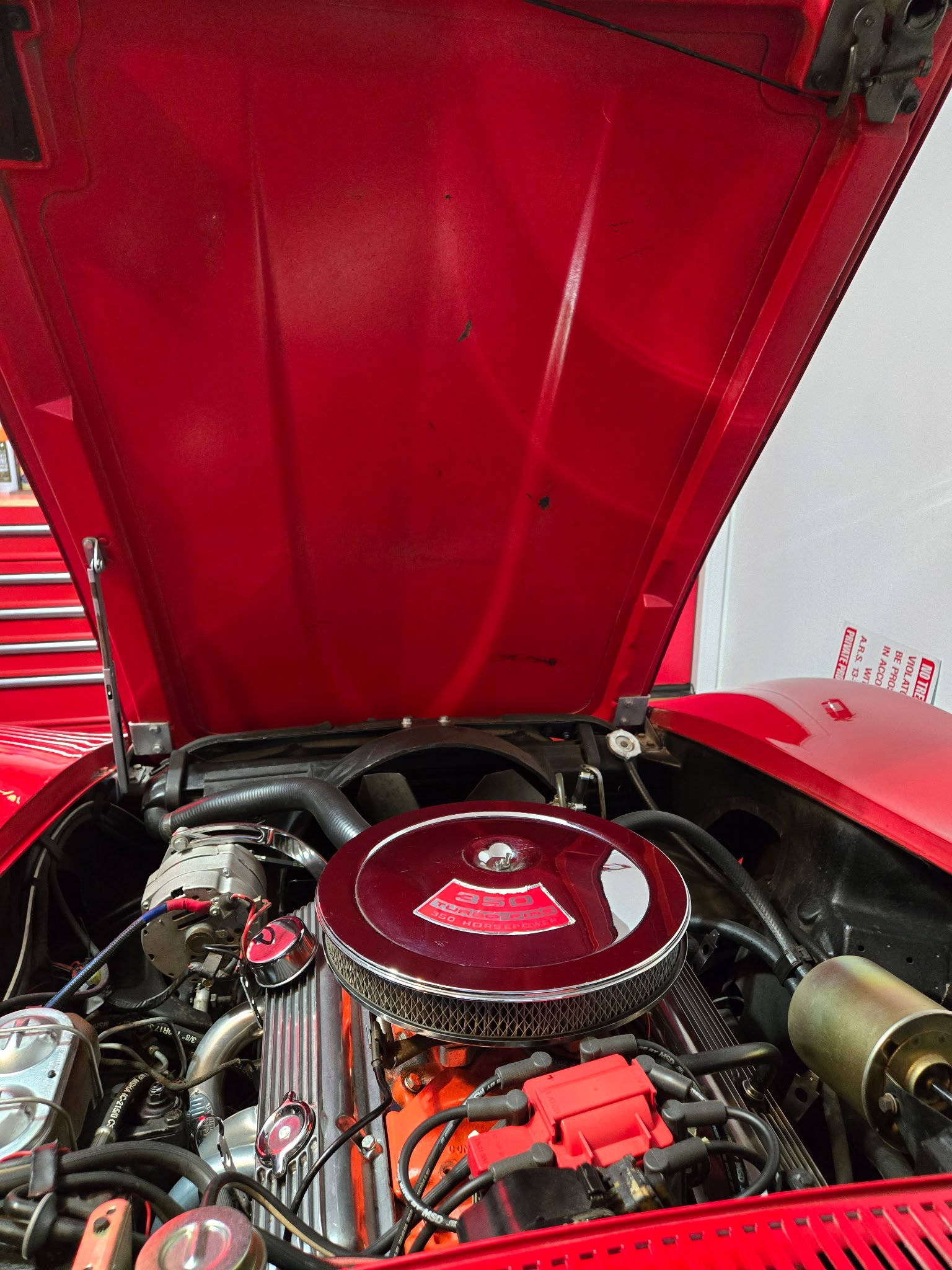 Classic red car engine bay with detailed chrome air filter cover and red valve covers displayed at ShuBrews Garage Bar.